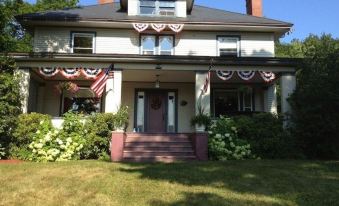 a large white house with a red door and american flags hanging from the awning at Taylor Edes Inn