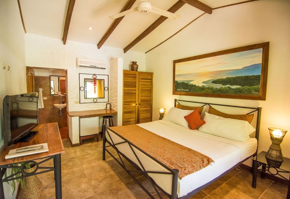a spacious bedroom with a large bed , a desk , and a painting on the wall at Conchal Hotel
