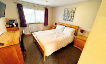 a bedroom with a large bed , wooden furniture , and purple curtains near a window with blinds at The Carrington Arms
