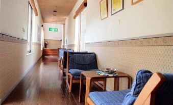 a hallway with wooden floors , white walls , and blue furniture , including tables and chairs , under the green arrow at Ganiba Onsen