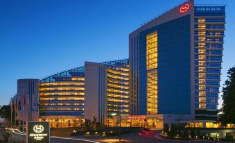 a large , modern hotel building with multiple floors and balconies , illuminated at night , surrounded by trees and other buildings at Sheraton Grand Adana