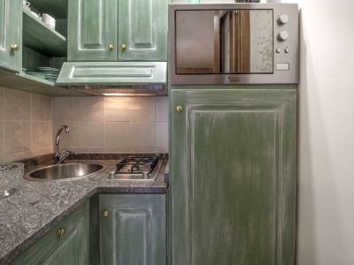a kitchen with green cabinets and a stainless steel microwave oven on the wall , next to a sink and oven at Messi