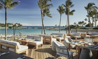 a wooden deck with white couches and chairs overlooks a pool and palm trees , surrounded by palm trees and the ocean at Four Seasons Resort Oahu at Ko Olina