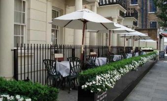 a row of outdoor dining tables with umbrellas and flowers , set in front of a building at Berjaya Eden Park London Hotel