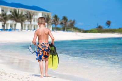 a young boy is walking on a sandy beach with his surfboard and paddle , preparing to go for a swim at Wyndham Reef Resort Grand Cayman