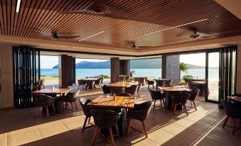 a large , open dining area with wooden tables and chairs , surrounded by a beautiful view of the ocean at Daydream Island Resort