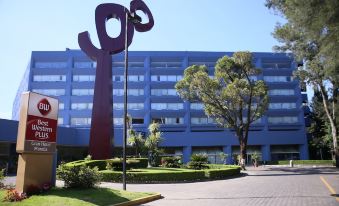 a large red sculpture stands in front of a blue building with trees and bushes around it at Best Western Plus Gran Hotel Morelia