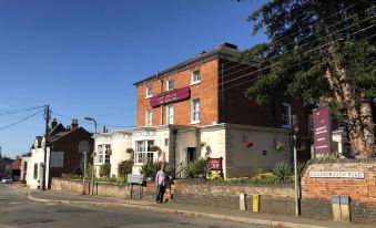 a brick building with a purple sign is next to a street with people walking at The Pytchley Inn