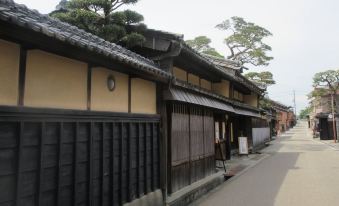 a traditional japanese building with black and yellow roofs , surrounded by trees and a cobblestone street at Just Inn Matsusaka Station
