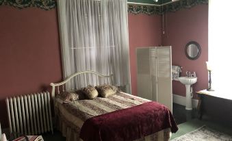 a bedroom with a bed , dresser , and window curtains is shown next to a bathroom at Shaw Mansion Inn