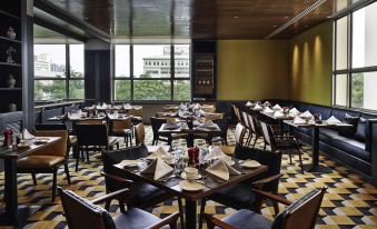 There is a restaurant with tables and chairs in front, and large windows that overlook the dining room area at Sofitel Saigon Plaza
