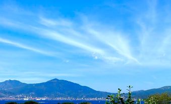 a clear blue sky with white clouds , mountains in the background , and a body of water in the foreground at Suite Home Porticcio