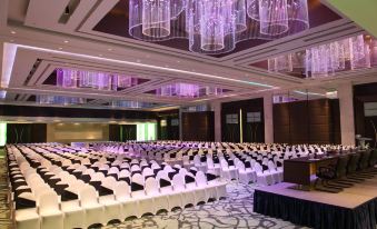 a large conference room with rows of chairs arranged in a symmetrical fashion , under chandeliers and purple lighting at Le Méridien Coimbatore