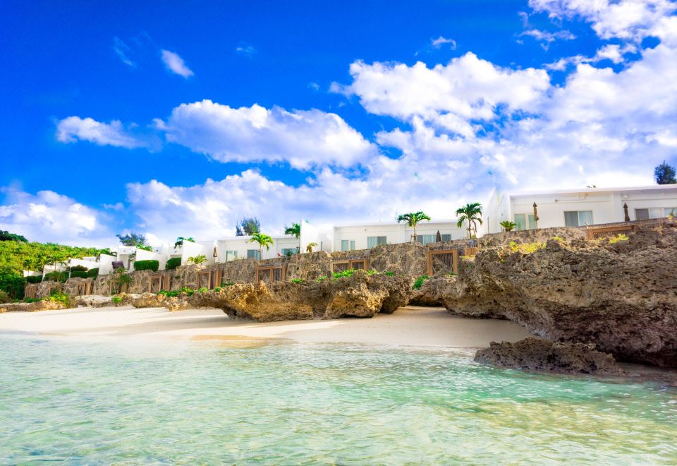 a beautiful beach scene with a large body of water in the foreground and a white building in the background at Crystal Villa Miyakojima Sunayama Beach