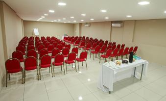 a large conference room with rows of red chairs and a white table at the front at Ibis Styles Piracicaba