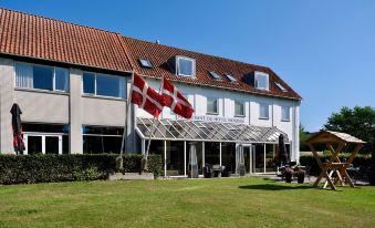 a large white building with a red and white flag on top , surrounded by green grass and trees at Hotel Norden