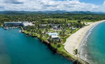 aerial view of a tropical resort with multiple buildings , swimming pools , and lush greenery near the ocean at The Pearl South Pacific Resort