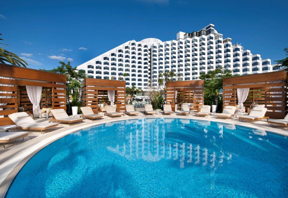 a large outdoor swimming pool surrounded by lounge chairs and umbrellas , with a hotel in the background at Crown Metropol Perth