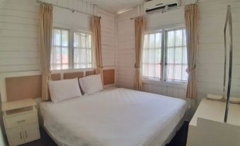 a large , well - made bed is situated in a room with wooden walls and windows , with white bedding and curtains at Marbella Twin Waterfall Resort Ciater