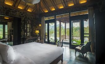 a luxurious bedroom with a king - sized bed , a chair , and a balcony overlooking a lake at Tam Coc Garden Resort