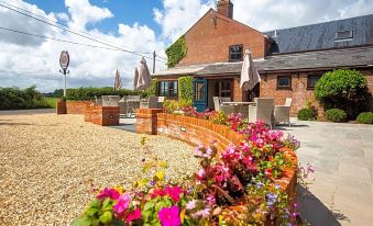 a brick house surrounded by a garden , with a paved patio and colorful flowers in the foreground at The Three Lions