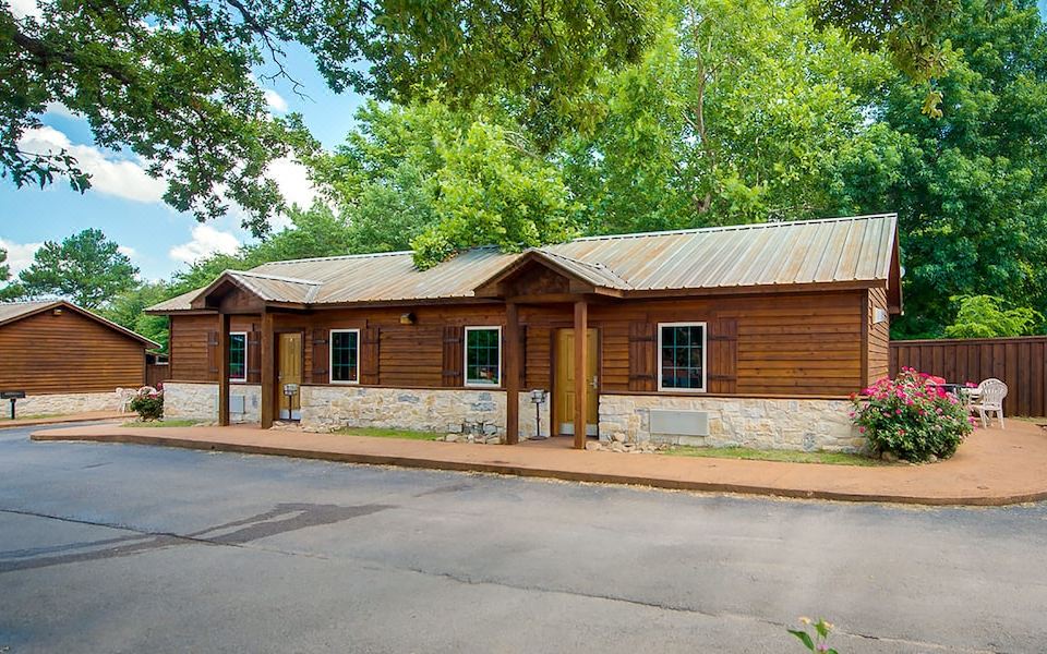 a wooden building with stone accents and a metal roof is situated in a wooded area at North Texas Jellystone Park
