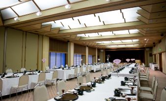 a large , well - lit banquet hall with multiple rows of tables and chairs set up for a formal event at Kaike Tsuruya