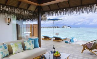 a wooden deck overlooking the ocean , with a couch and chairs on the deck for relaxation at Pullman Maldives All-Inclusive Resort