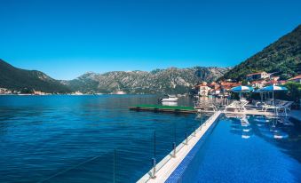 a beautiful blue lake with mountains in the background , and a boat floating on the water at Heritage Grand Perast by Rixos