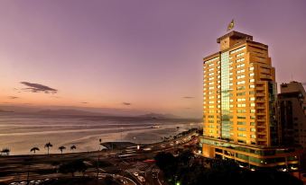 a tall building with a green flag on top is located near the ocean at sunset at Majestic Palace Hotel