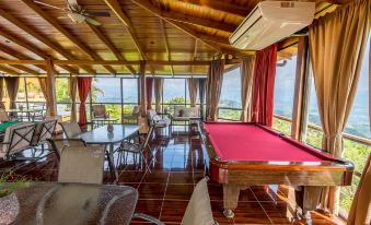 a room with a pool table and couches , overlooking the ocean , with red curtains at Barons Resort