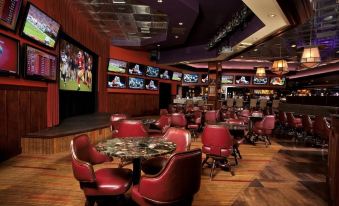 a large , well - lit room with multiple tables and chairs , a bar , and multiple televisions displaying sports games at Carson Valley Inn