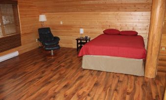 a cozy bedroom with wooden walls , a bed with red bedding , and a black chair at Beaver Lake Resort