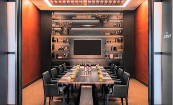 a long wooden table with black chairs is set up in a room with red walls and shelves at Rydges Wellington Airport, an EVT hotel