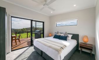 a modern bedroom with a large bed , white bedding , and sliding glass doors leading to an outdoor deck at Glenworth Valley Outdoor Adventures