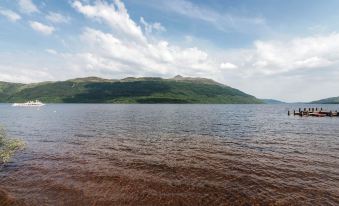 a serene lake with clear water and a mountain in the background , under a blue sky dotted with clouds at The Tarbet Hotel