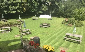 a lush green lawn with picnic tables and umbrellas set up for outdoor dining , surrounded by trees and flowers at Stanley Arms Hotel