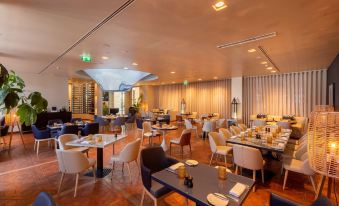 a modern restaurant with multiple dining tables and chairs , some of which are occupied by people at Hilton Vilamoura As Cascatas Golf Resort & Spa