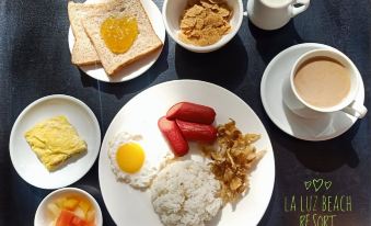 a plate of breakfast food , including eggs , rice , and toast , is displayed on a table with various dishes and drinks at La Luz Beach Resort