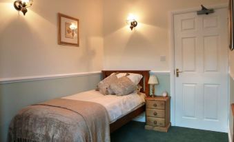 a cozy bedroom with a single bed , a nightstand , and a door leading to another room at The Bell Inn