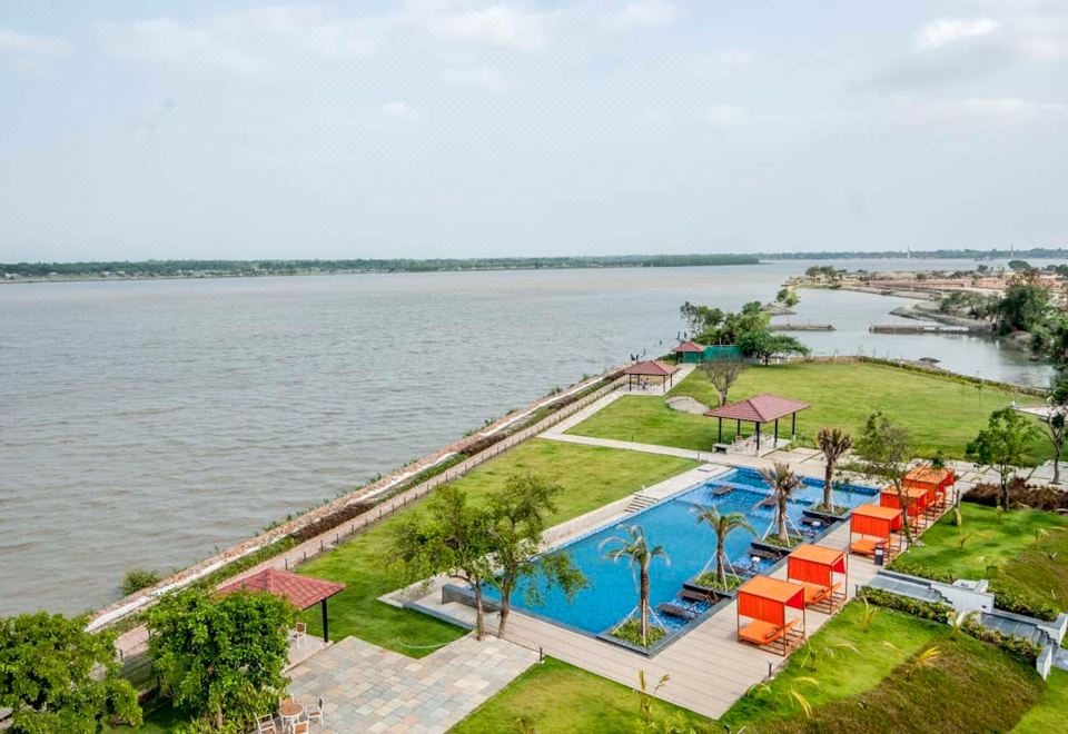 a large pool is surrounded by lounge chairs and palm trees , with a view of the water at Hotel Sonar Bangla Taki