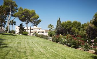 a large house is situated on a hillside , surrounded by lush green grass and trees at Invisa Hotel Club Cala Blanca