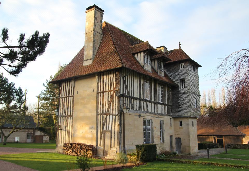 a large , old - fashioned house with a wooden roof and stone foundation is surrounded by greenery at Les Manoirs des Portes de Deauville - Small Luxury Hotel of the World