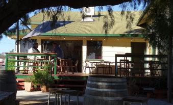 a small house with a green roof , surrounded by trees and a wine barrel in the courtyard at Gowrie Hotel Motor Inn