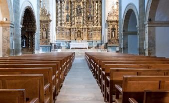 an empty church with rows of wooden pews , a large altar in the background , and blue carpeted floor at Parador Monasterio de Corias