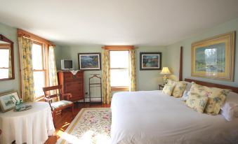 a bedroom with a large bed , two nightstands , and a chair , all lit by sunlight coming through the window at Highland Lake Inn