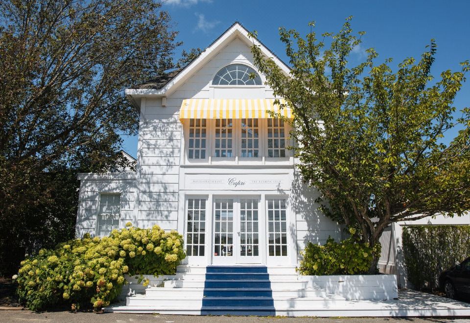 a white house with a yellow and white striped awning , surrounded by green bushes and trees at Capri Southampton