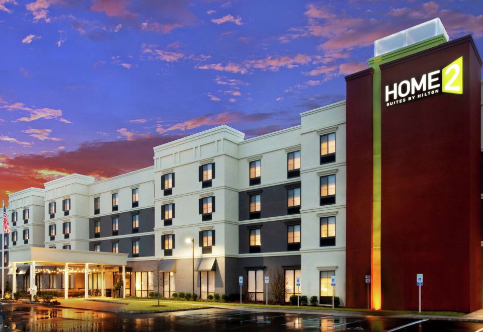 a hotel building with its name displayed on it , located in a city setting at dusk at Home2 Suites by Hilton Long Island Brookhaven