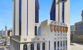 a large , modern building with multiple towers and a central archway is surrounded by a cityscape at Hilton Suites Makkah