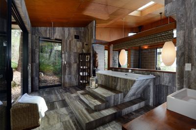 a luxurious bathroom with a large bathtub , wooden walls , and stone steps leading to the shower area at Spicers Sangoma Retreat